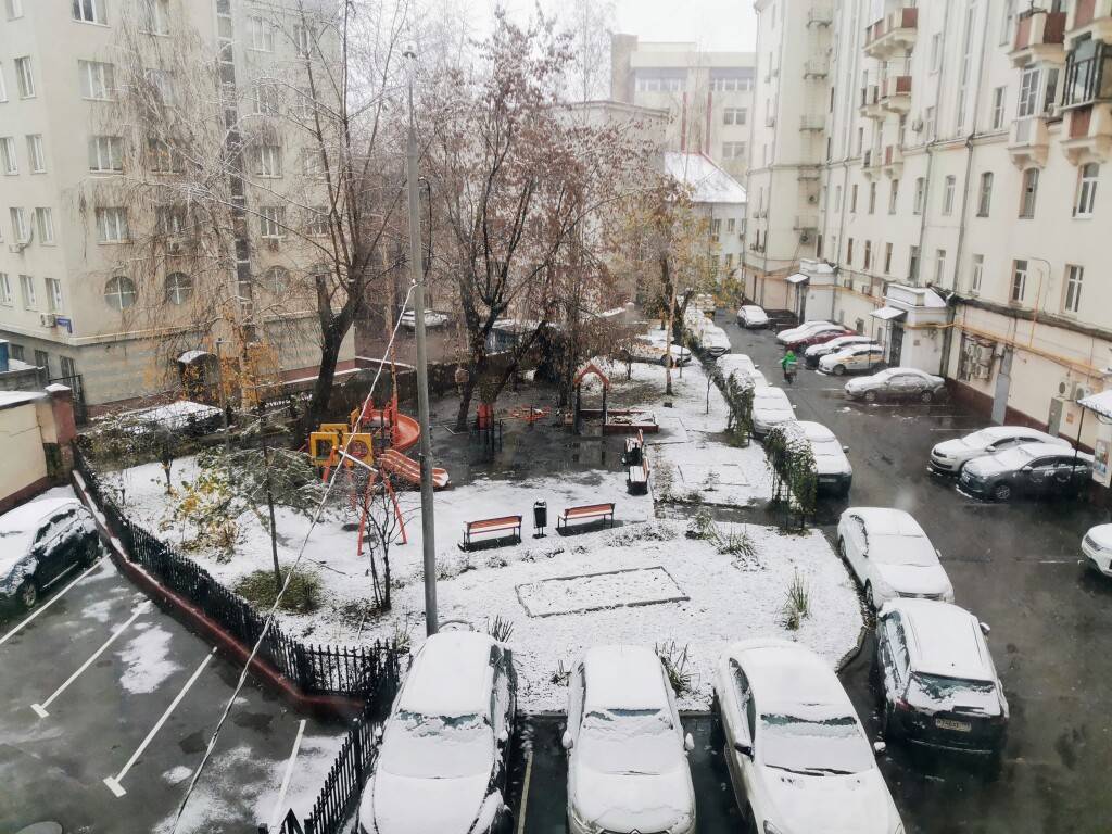 Снежный день в дворе советской многоэтажки: скользкий асфальт, снег на детской площадке и машинах