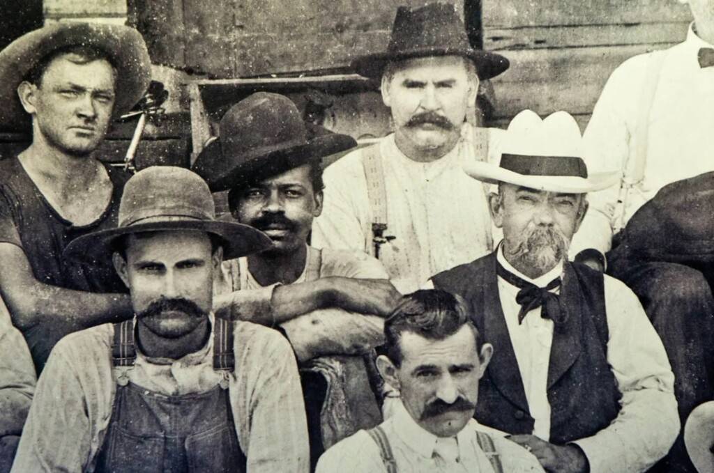 Рабочие в кепках и подтяжках у деревянного сарая, 1900-е