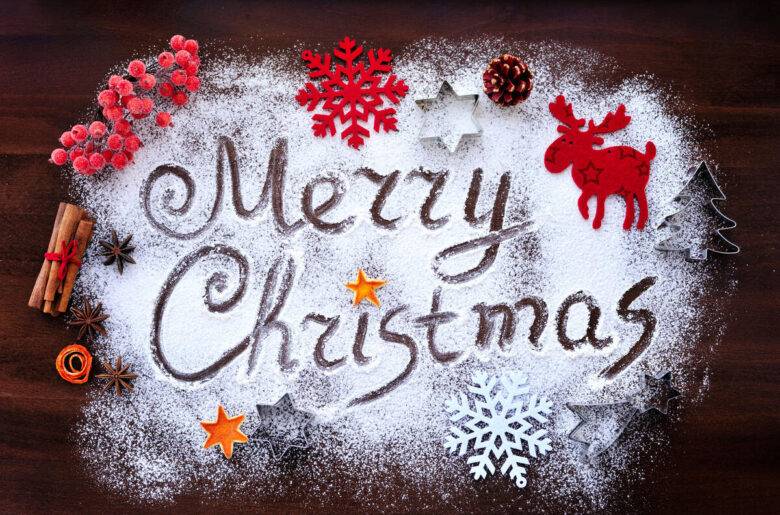 Сахарная надпись «Merry Christmas» с еловыми шарами и корицей на темном дереве
