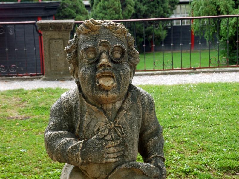 Каменная фигура в саду Зальцбурга: кряхтящий мужчина с шляпой и очками