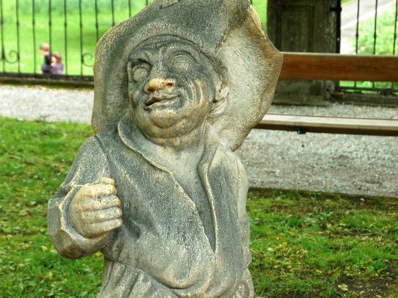 Каменная фигура в парке Зальцбурга: шляпа, усмешка, сундук