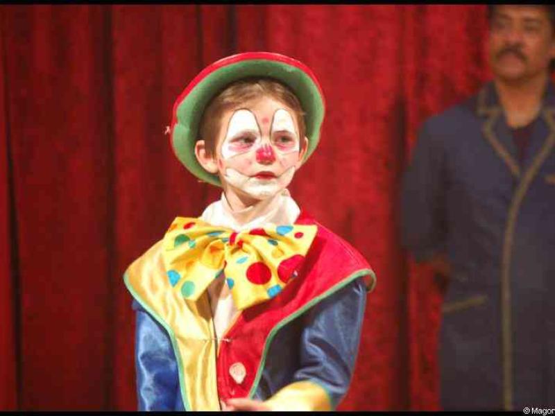 Клоун в шляпе с зелёной окантовкой на фоне красного занавеса в Cirque Бельгии