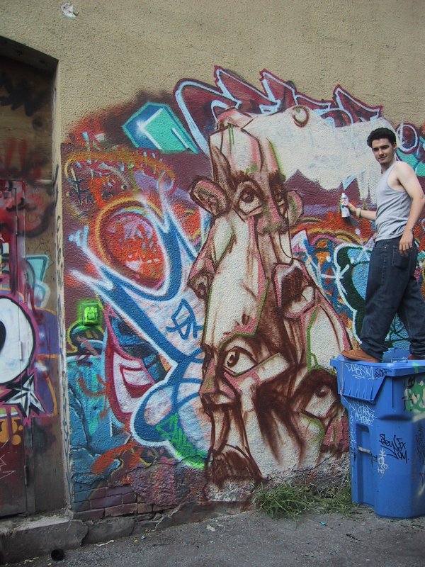 416 Grafitti Expo, Канада: художник на синем баке перед муралом с лицом и кричащими цветами