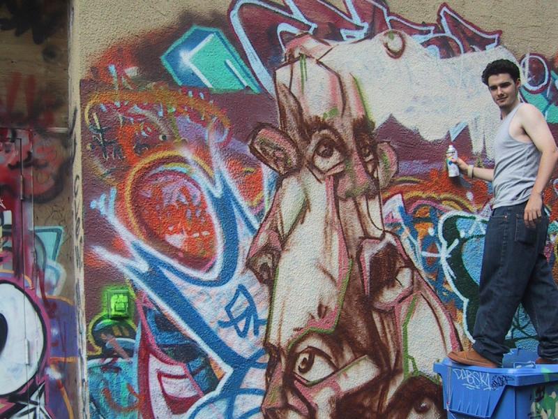 416 Grafitti Expo, Канада: художник на синем баке перед муралом с лицом и кричащими цветами