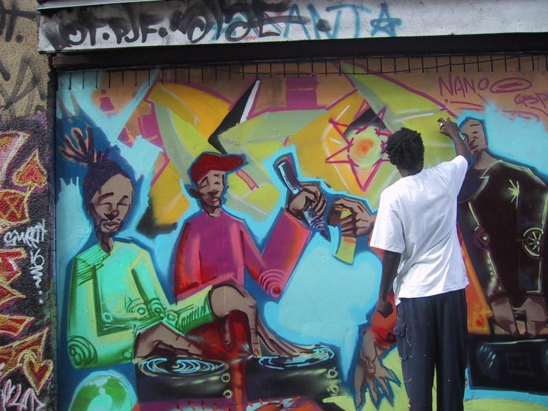 416 Graffiti Expo, Канада: художник в белой футболке добавляет детали к яркой стене с персонажами