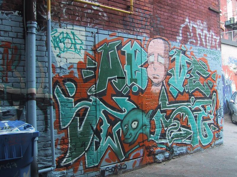 416 Grafitti Expo, Канада: кирпичная стена с зелёно-оранжевым граффити и лицом в стиле мультфильма