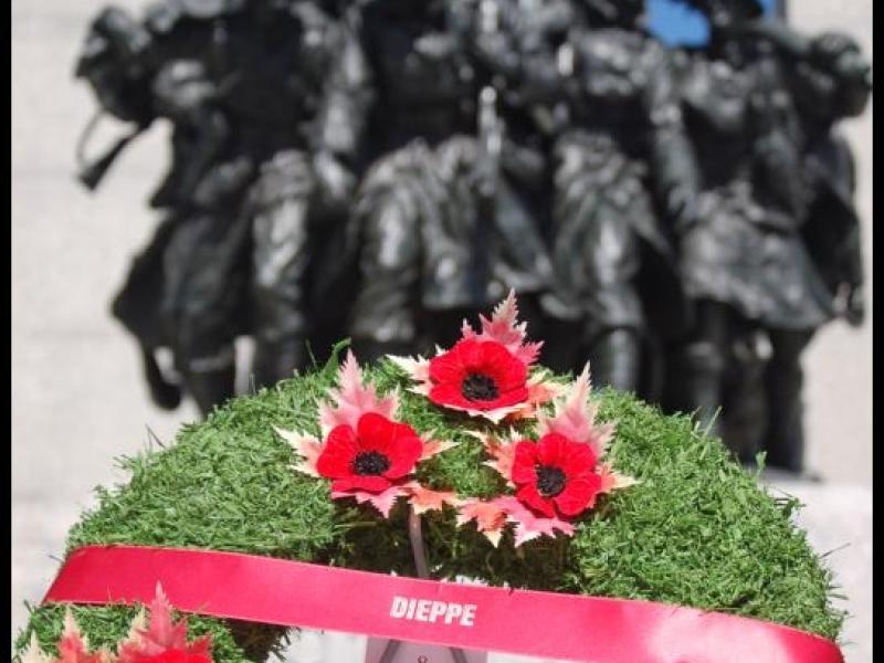 Венок с красными маками и лентой с надписью Dieppe перед памятником солдатам