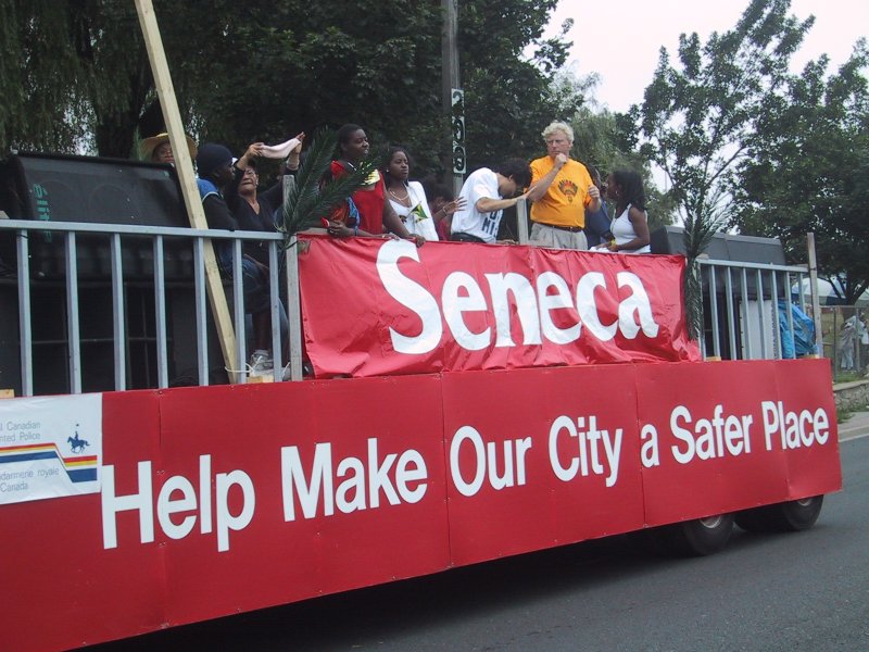 Caribana 2003 в Торонто: красный фургон с баннером «Seneca» и призывом «Help Make Our City a Safer Place»