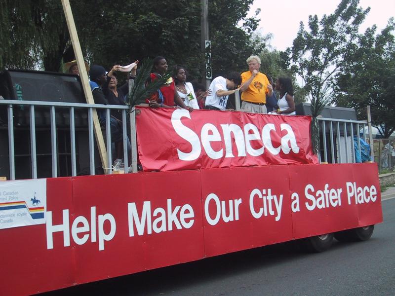Caribana 2003 в Торонто: красный фургон с баннером «Seneca» и призывом «Help Make Our City a Safer Place»