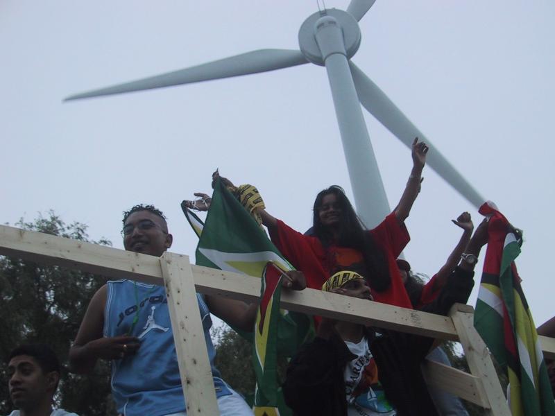 Caribana 2003, Канада: ветряная турбина за деревянной платформой с флагами Суринама