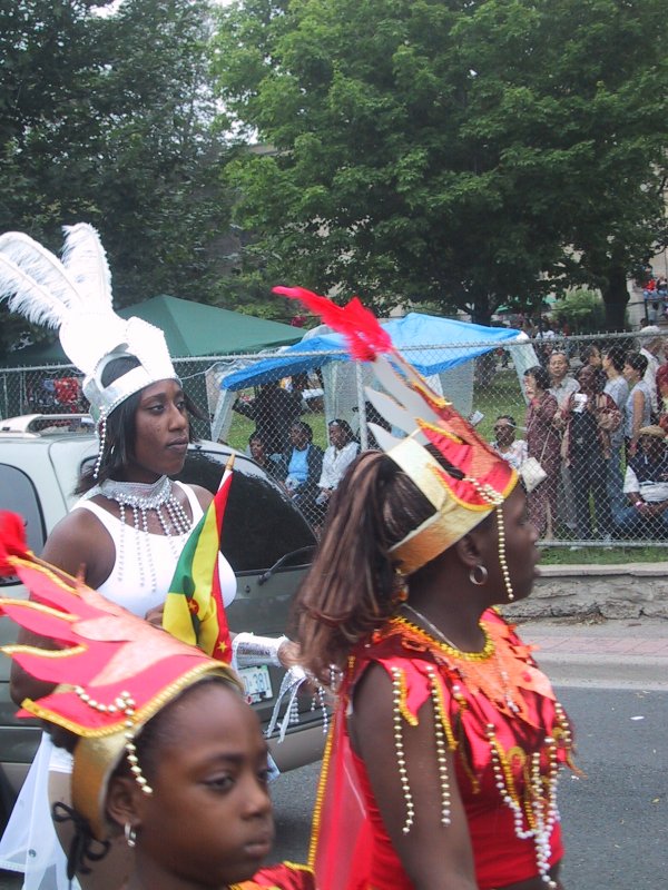 Caribana 2003 в Торонто: танцующие в красно-золотых костюмах с перьями и флагом Гренады