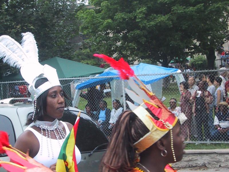 Caribana 2003 в Торонто: танцующие в красно-золотых костюмах с перьями и флагом Гренады
