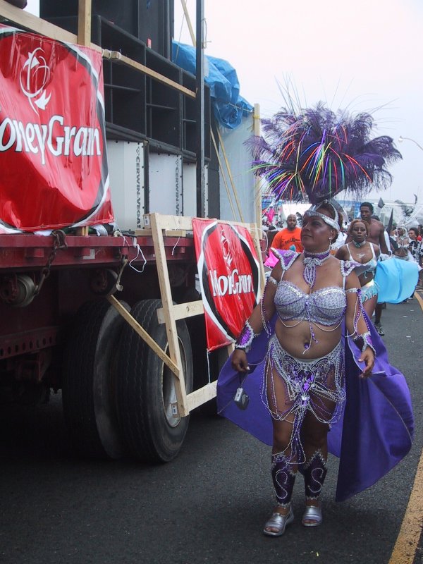 Caribana 2003 в Торонто: танцующая участница в фиолетовом костюме у грузовика с баннером «HoneyGrain»