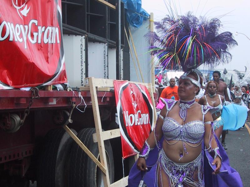 Caribana 2003 в Торонто: танцующая участница в фиолетовом костюме у грузовика с баннером «HoneyGrain»