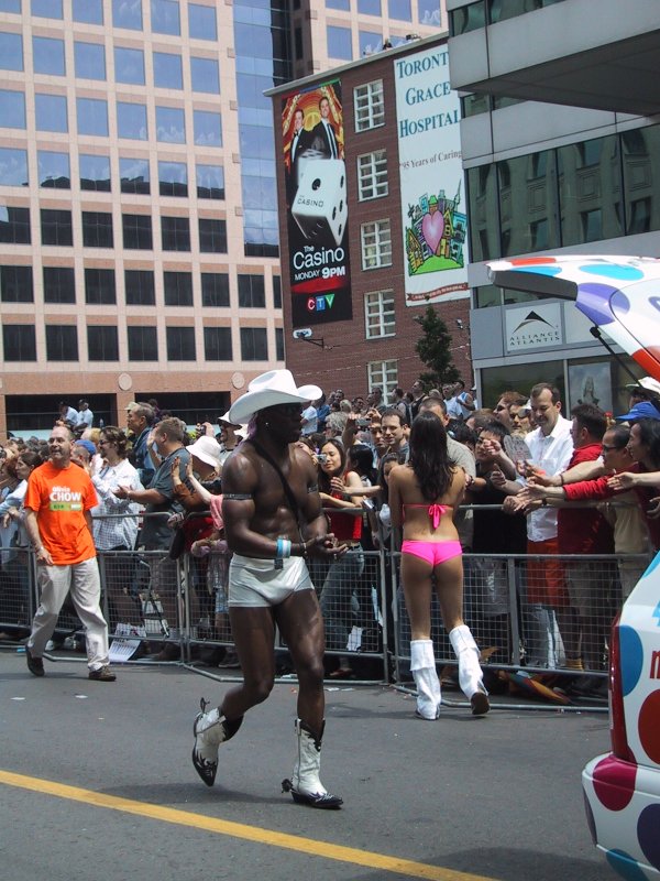 Торонто, Pride Parade, 27 июня 2004: мужчина в белом ковбойском шляпе и сапогах, женщина в розовом бикини и высоких белых чулках проходят мимо толпы у здания Toronto Grace Hospital