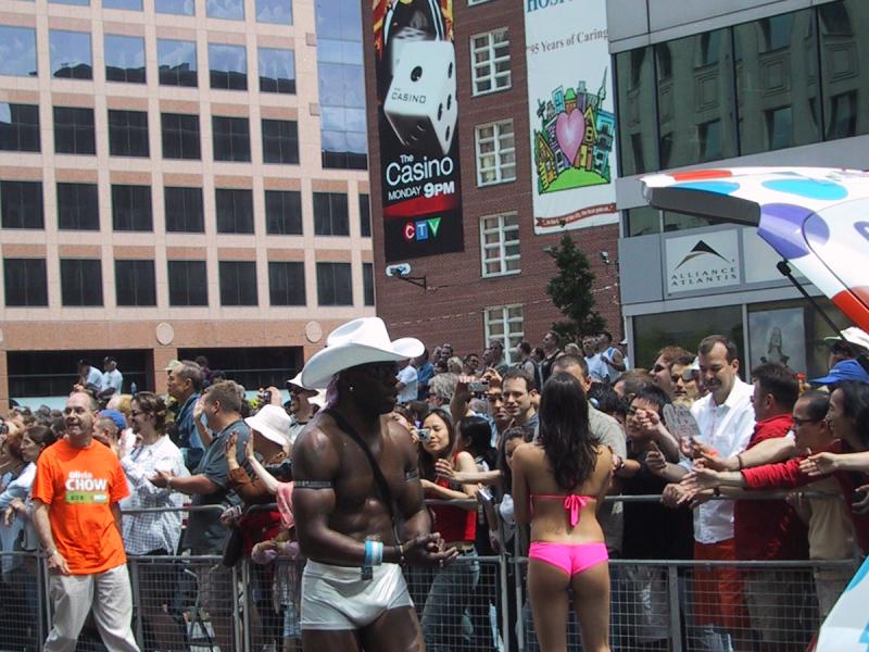 Торонто, Pride Parade, 27 июня 2004: мужчина в белом ковбойском шляпе и сапогах, женщина в розовом бикини и высоких белых чулках проходят мимо толпы у здания Toronto Grace Hospital