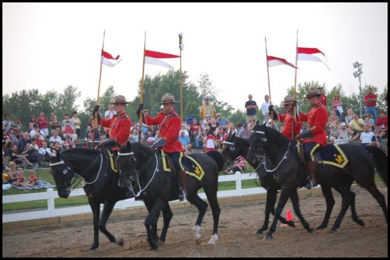 RCMP в красных мундирах на конях с флагами Канады в парке