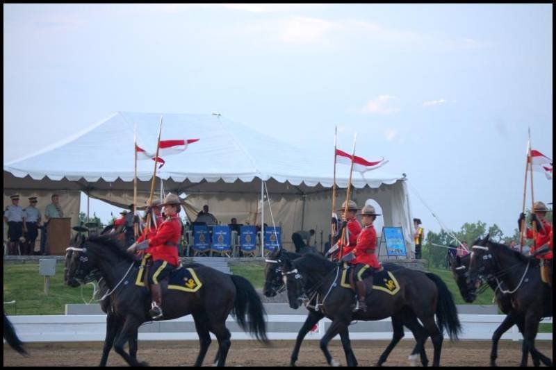 RCMP в красных мундирах на черных лошадях у белой палатки в Канаде