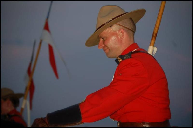 RCMP в красной форме на закате у флага Канады