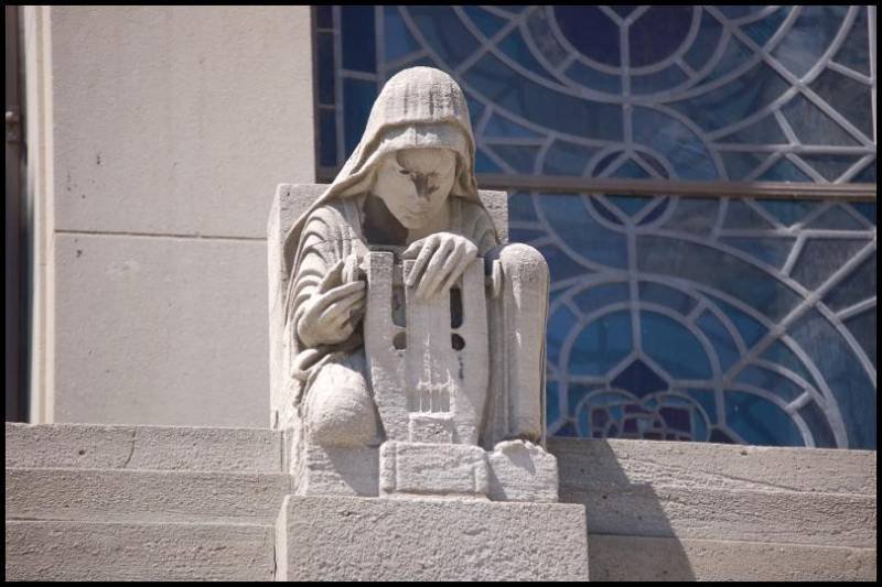 Каменная скульптура молящегося человека у ступеней здания с витражом
