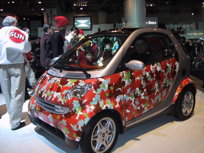 Маленький автомобиль Smart с узором из кленовых листьев на выставке автомобилей