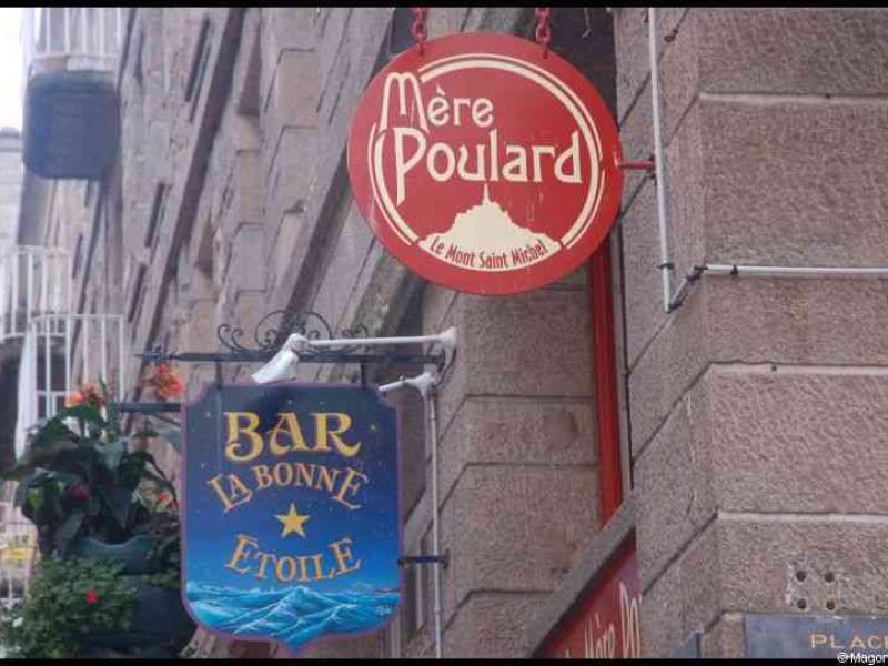 Красная круглая вывеска 'Mère Poulard' и синяя вывеска 'Bar La Bonne Etoile'