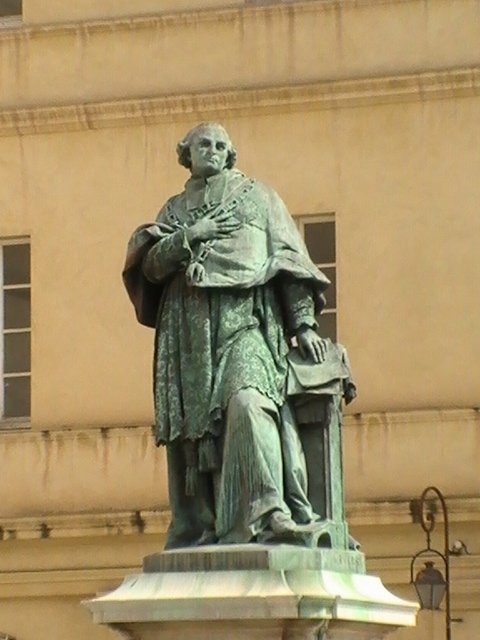 Памятник в Ajaccio, 2008: бронзовая фигура в плаще с крестом на груди у основания светлого фасада