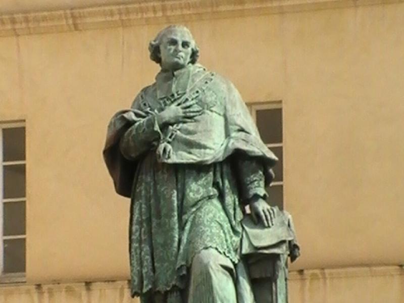 Памятник в Ajaccio, 2008: бронзовая фигура в плаще с крестом на груди у основания светлого фасада