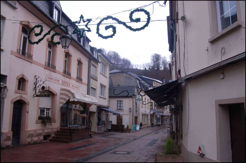 Clervaux, Люксембург: узкая улочка с витринами и зелёными гирляндами