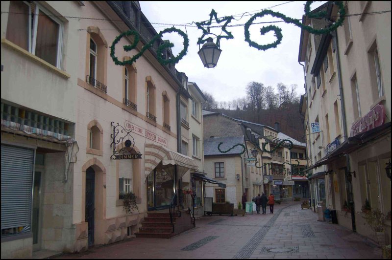 Узкая улочка в Clervaux, Люксембург: фонарь и зелёные гирлянды над бутиком Dimmer