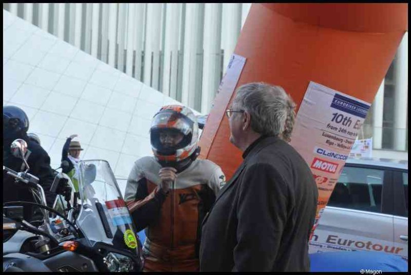 Eurobikers 2012 в Люксембурге: мотоциклист в шлеме с оранжевыми акцентами разговаривает с мужчиной у арки