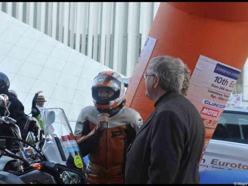 Eurobikers 2012 в Люксембурге: мотоциклист в шлеме с оранжевыми акцентами разговаривает с мужчиной у арки