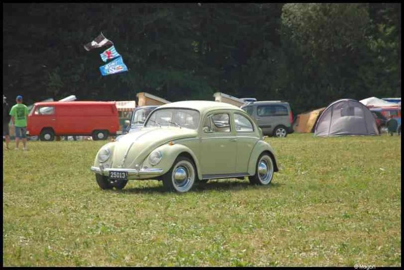 Зелёный классический Volkswagen Beetle на лужайке с автотехникой и палатками
