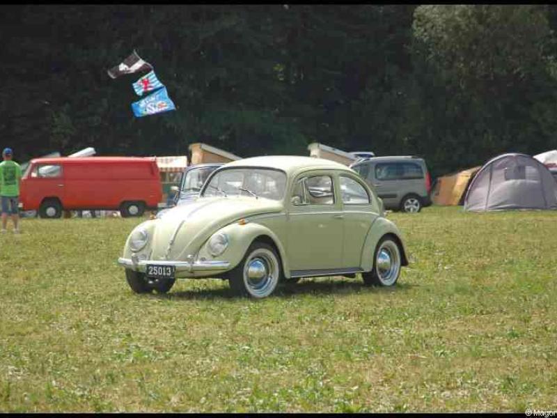 Зелёный классический Volkswagen Beetle на лужайке с автотехникой и палатками