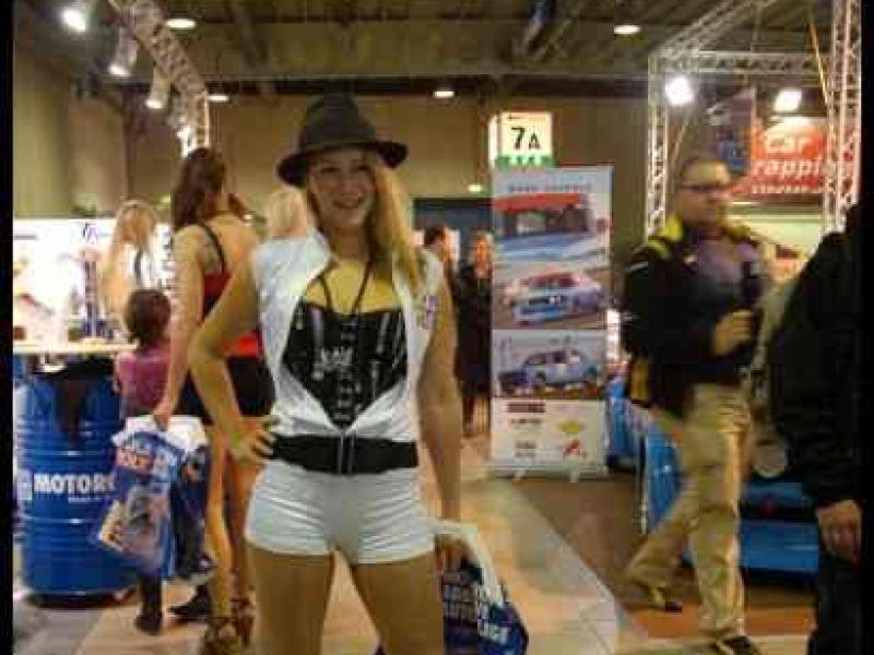 Motorshow 2010 в Люксембурге: женщина в шляпе и белом костюме у стойки с маслом