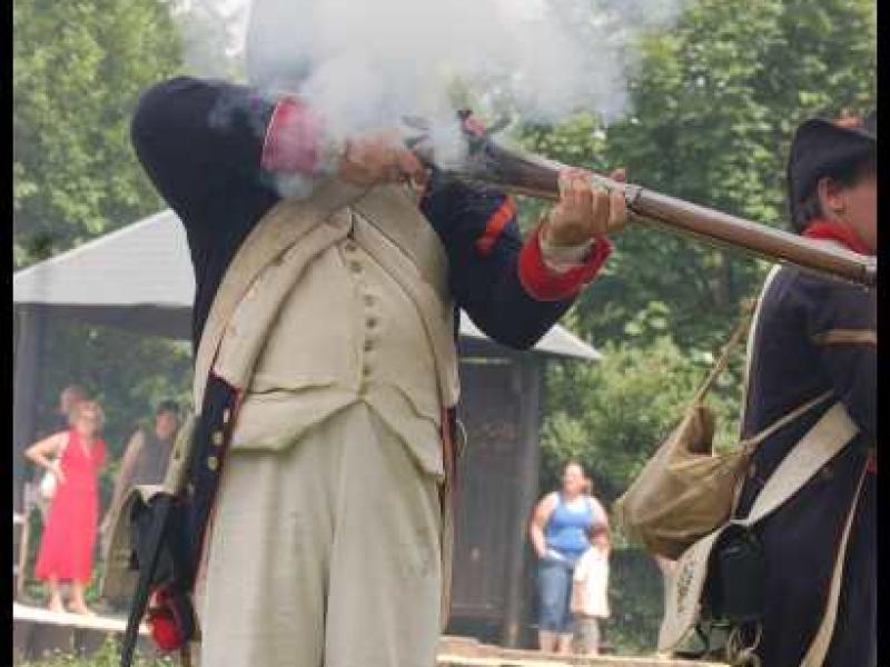 Napoleonic Bivouac в Люксембурге: солдат в белых штанах и куртке с красными манжетами поднимает ружьё