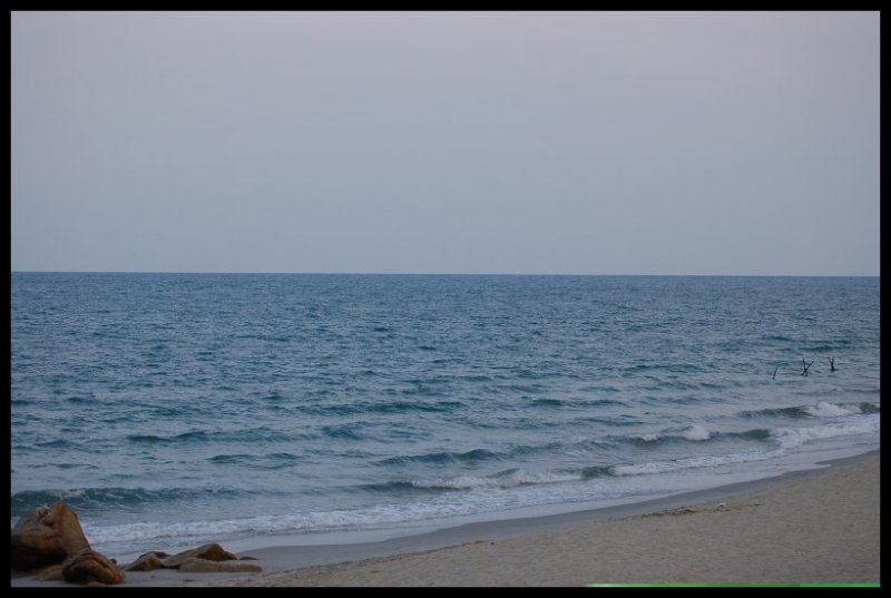 Песчаный пляж с камнями у кромки моря в сумерках