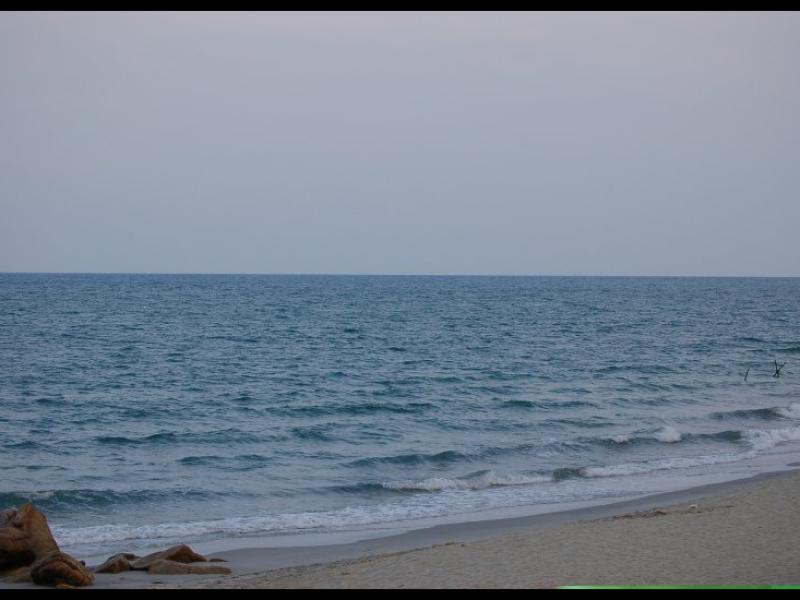 Песчаный пляж с камнями у кромки моря в сумерках