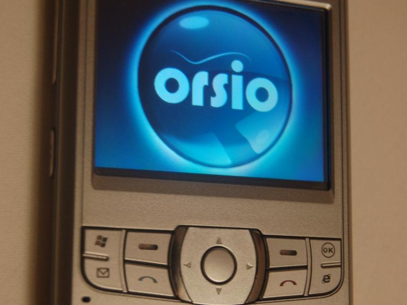 Orsio P745 на стене — серебристый смартфон с QWERTY-клавиатурой и логотипом в центре экрана
