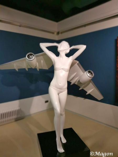 Белая скульптура женской фигуры с самолетными крыльями на выставке