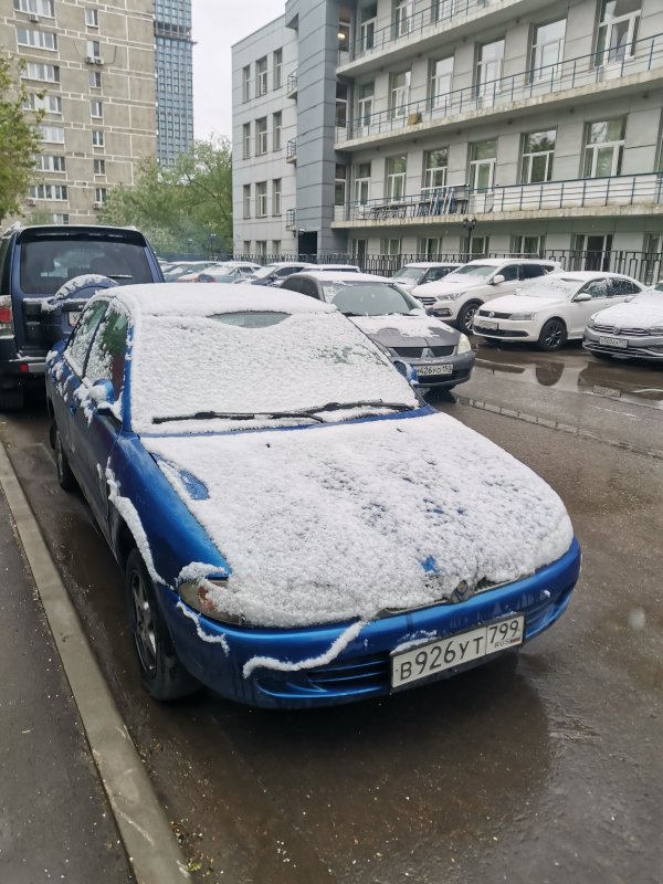 Москва, 7 мая 2024: снег на синем «Митсубиси» у подъезда в типовой панельной застройке