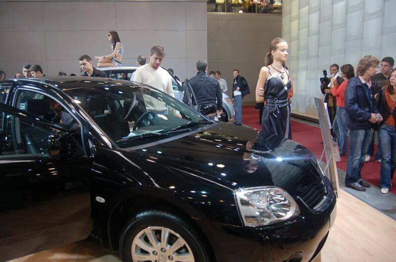 Черный автомобиль на автосалоне с посетителями и манекеном