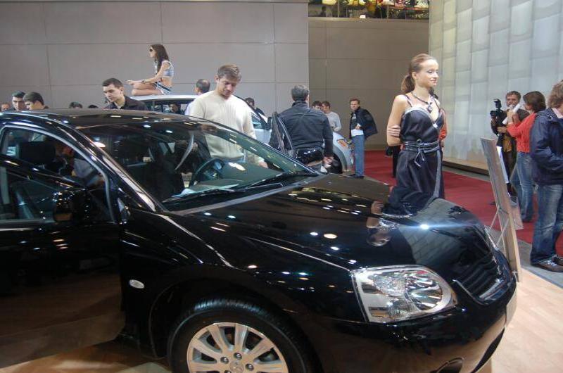 Черный автомобиль на автосалоне с посетителями и манекеном