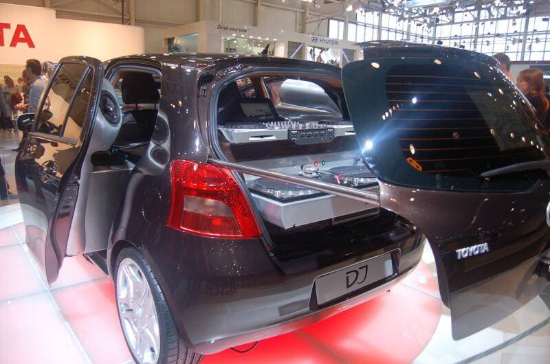 Чёрный Toyota Yaris с открытыми дверями и аудиосистемой в багажнике на автосалоне