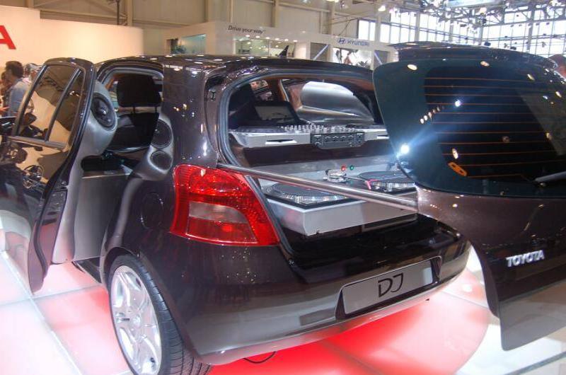 Чёрный Toyota Yaris с открытыми дверями и аудиосистемой в багажнике на автосалоне