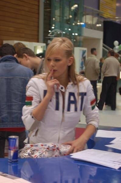 Motorshow 2006: женщина в белой куртке с надписью «HAT» и флагами на рукавах за синим столом