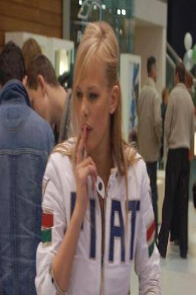 Motorshow 2006: женщина в белой куртке с надписью «HAT» и флагами на рукавах за синим столом