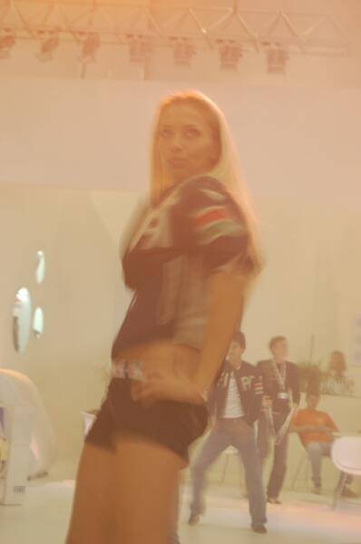 Motorshow 2006: блондинка в куртке с эмблемой на фоне размытых участников выставки