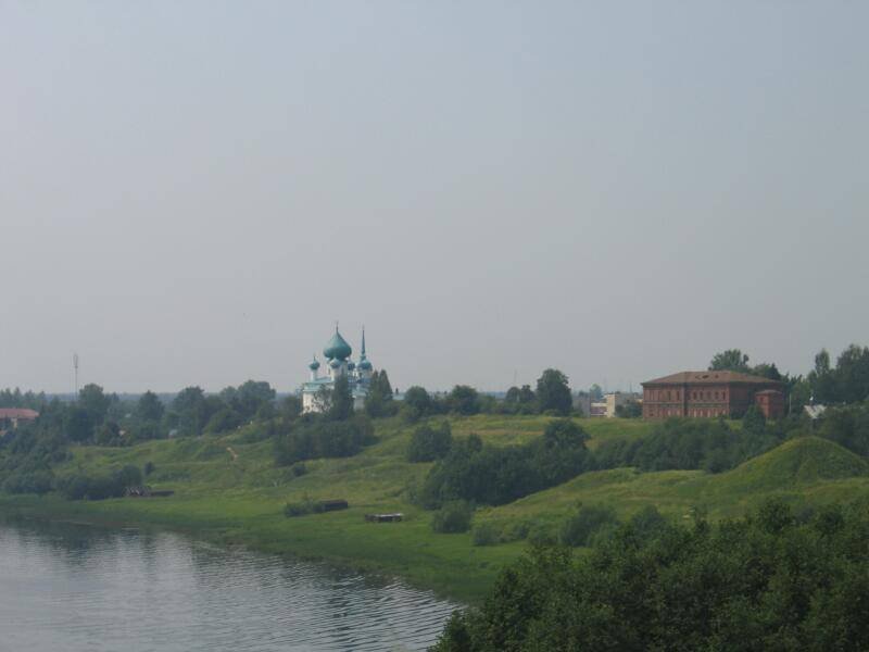 Старая Ладога, 2006: зелёный холм у воды с белокаменной церковью и красно-кирпичным зданием