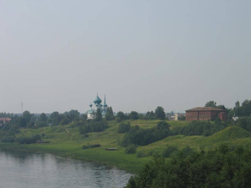 Старая Ладога, 2006: зелёный холм у воды с белокаменной церковью и красно-кирпичным зданием
